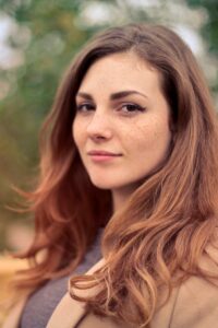 A young woman with long hair smiles confidently for an outdoor portrait session.
